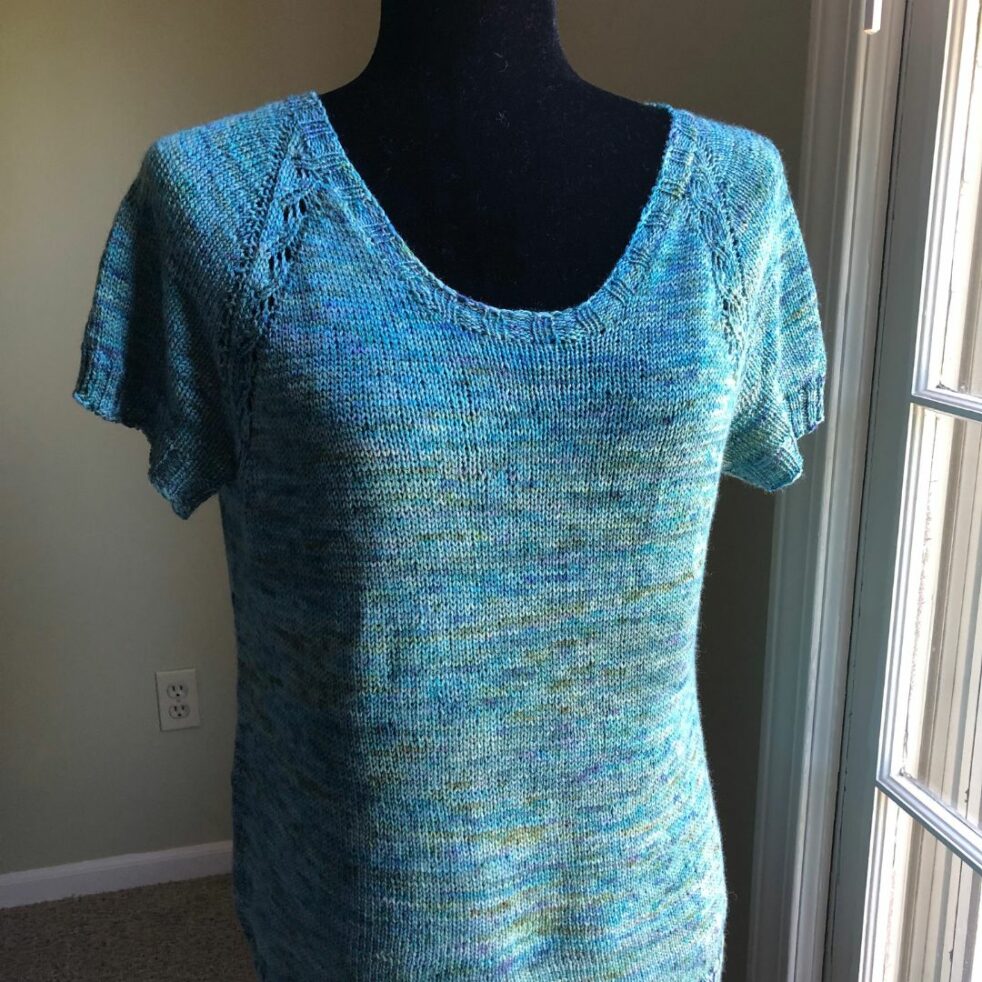 A blue knit tee, mostly stockinette, featuring lace details at the shoulders